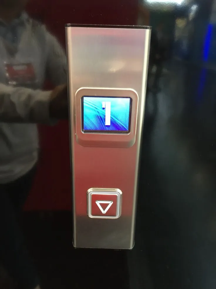 Brushed stainless steel elevator landing operating panel with blue LCD floor indicator and single illuminated down call button in a commercial lobby