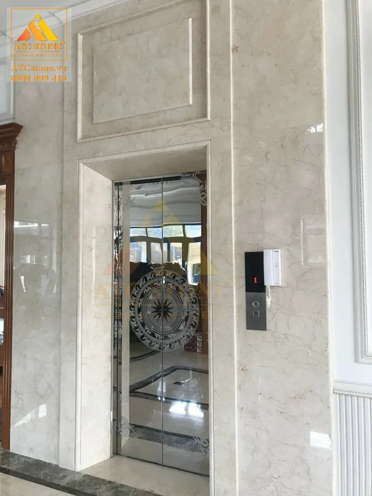 Mirror stainless steel elevator landing door with etched medallion and floral border in a marble-clad villa lobby, Lahore home lift