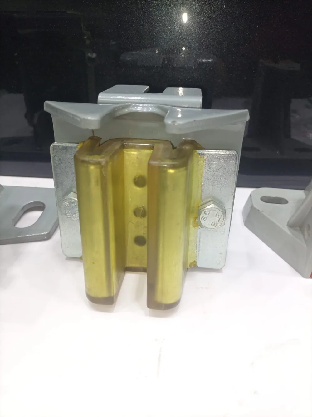Elevator guide shoe with amber nylon liner clamped over a machined T-profile guide rail head showing jaw-to-rail clearance set for EN 81-20 guiding requirements