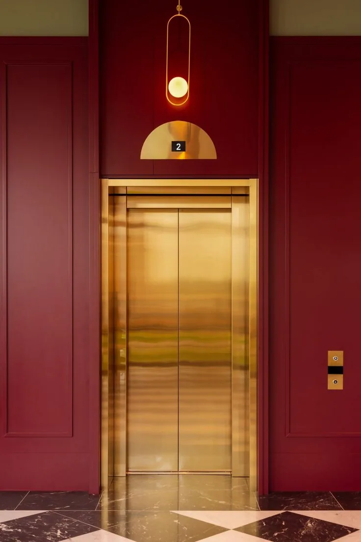 Gold mirror titanium coated stainless steel elevator landing door with brass header and floor number indicator in a luxury lobby
