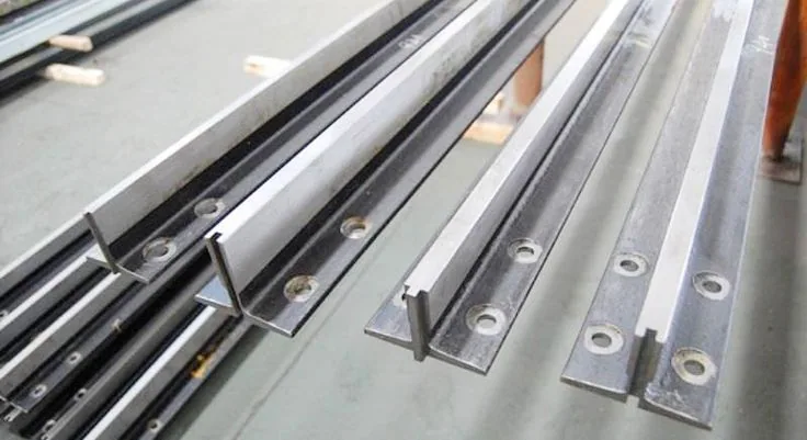 Cold-drawn and machined elevator guide rails laid out in a workshop showing rail head profiles, base flanges and bracket fixing holes before alignment to plus-minus 0.5 mm plumb